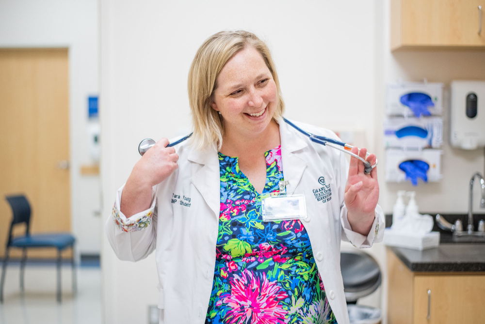 Tara Young laughs while holding a stethoscope and dressed in a lab coat
