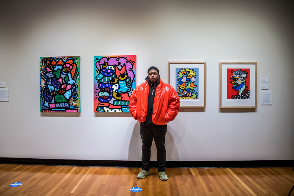 man in puffy red jacket stands in front of colorful artwork in the art gallery