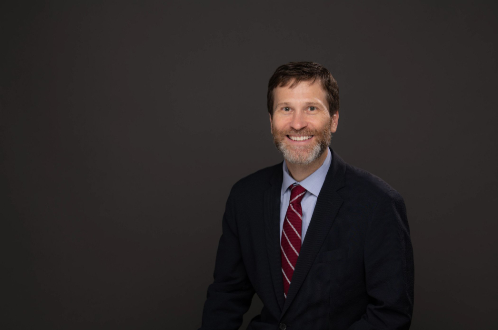 Sean Lancaster in dark suit coat and light blue shirt, striped tie