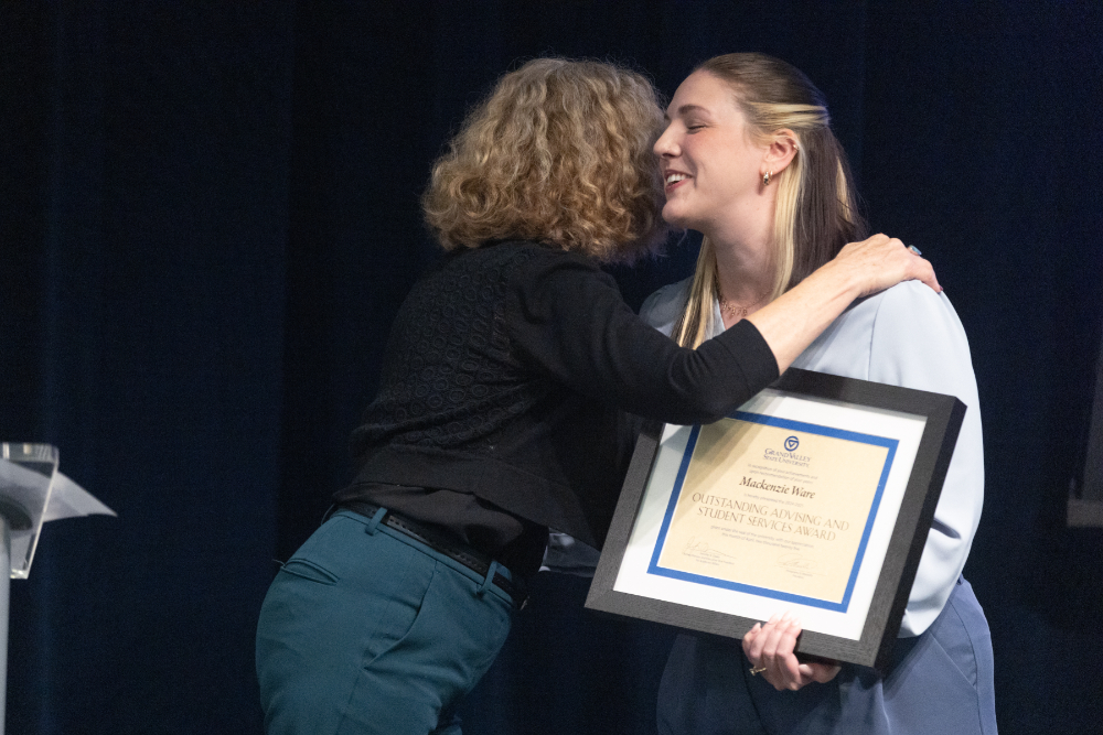 Mackenzie Ware holds a certificate in a frame while being hugged by Jennifer Drake