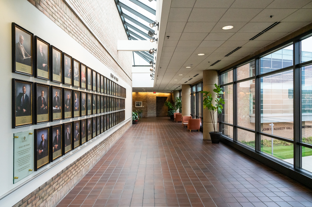portraits on a wall inside the Eberhard Center down a hallway with windows on the other side