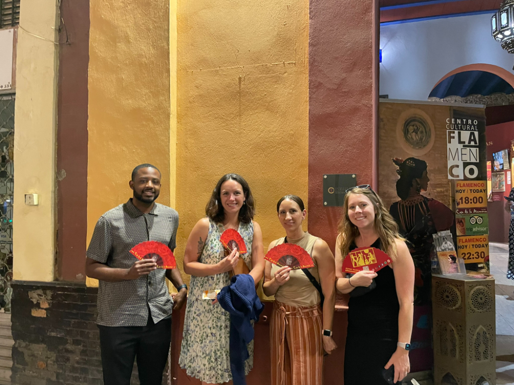 four people standing outside building holding red paper fans