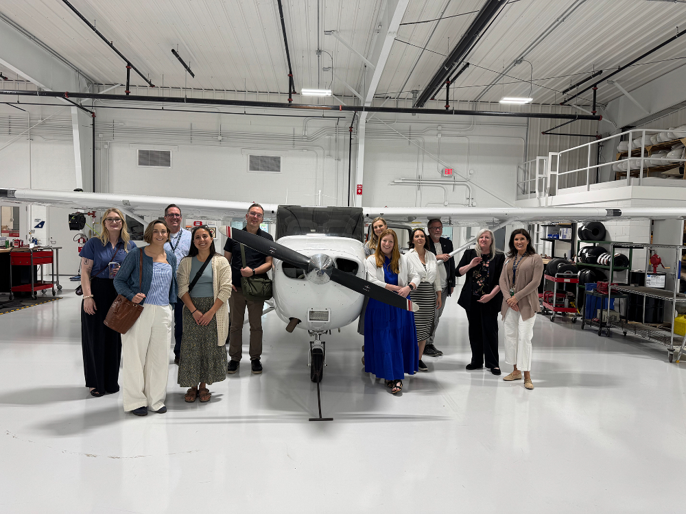 in an airplane hanger, two groups of people stand on either side of a small airplane