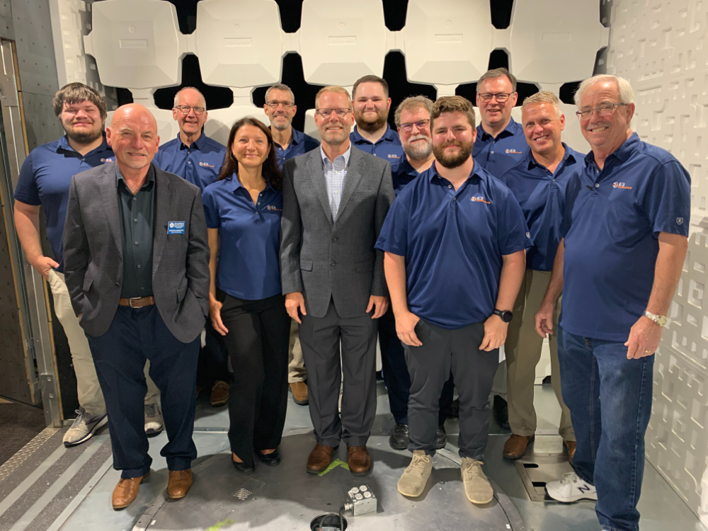 two rows of people standing for photo, most in blue polo shirts, two men in front in suits
