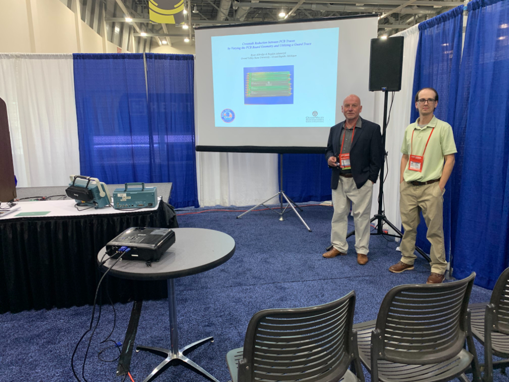 two people standing at convention booth with blue and white draping behind them