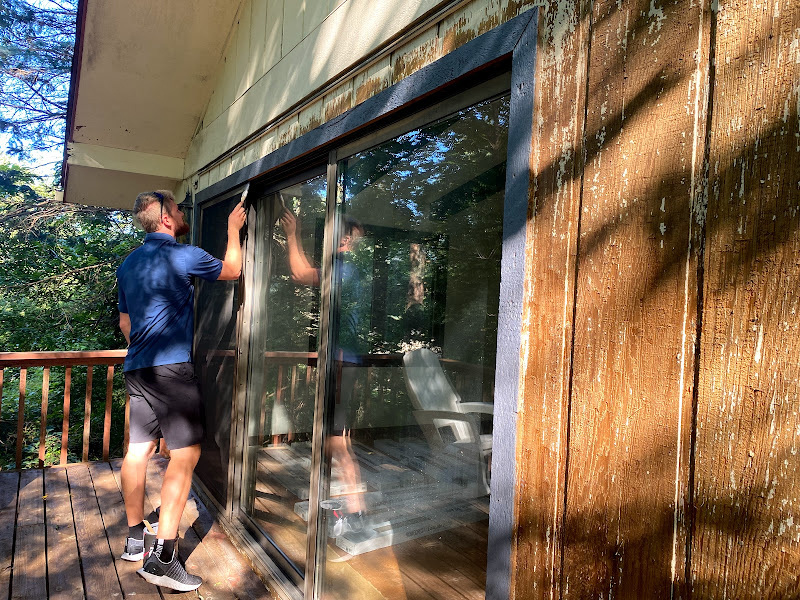 a student stands outside on a deck to paint the exterior of a sliding door