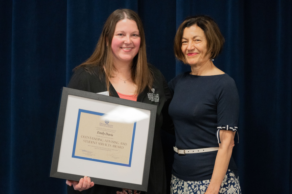 two people standing next to each other, person on left holds large framed certificate