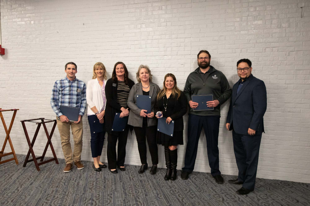 seven people stand next to a white wall