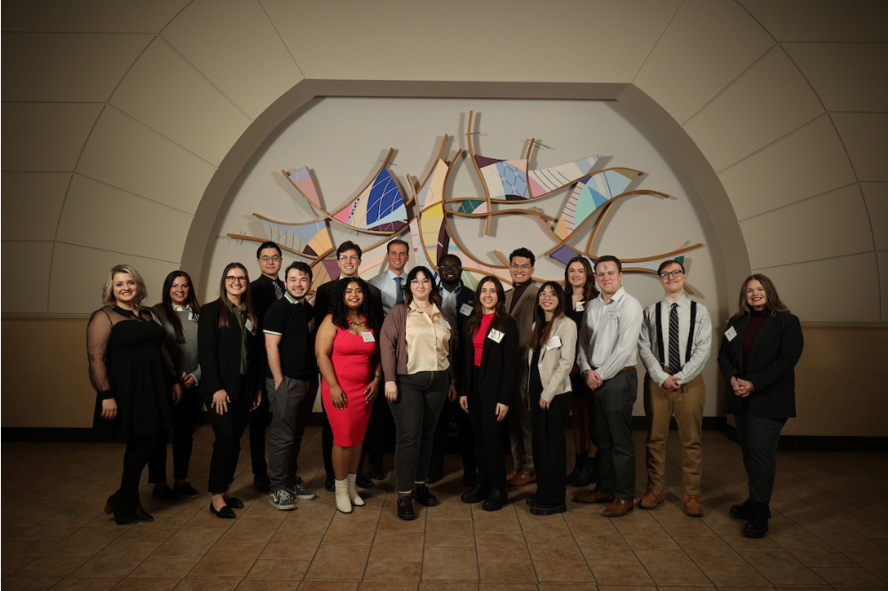 two rows of students posing in front of artwork on wall at the DeVos Center