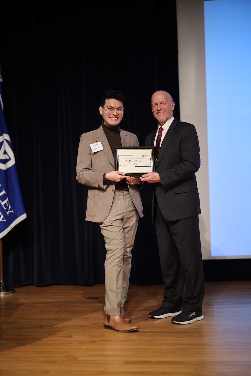 student Jowei Yek in light brown suit accepts a certificate from Jeff Potteiger, who is dressed in a dark suit