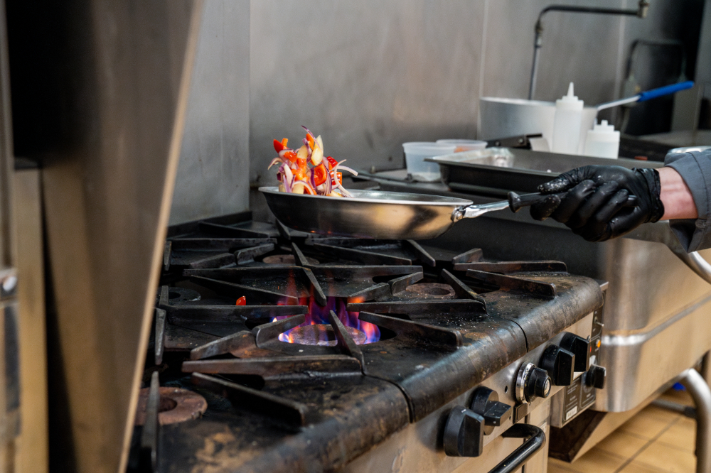 sauce pan of vegetables on stove being lifted by chef's hand