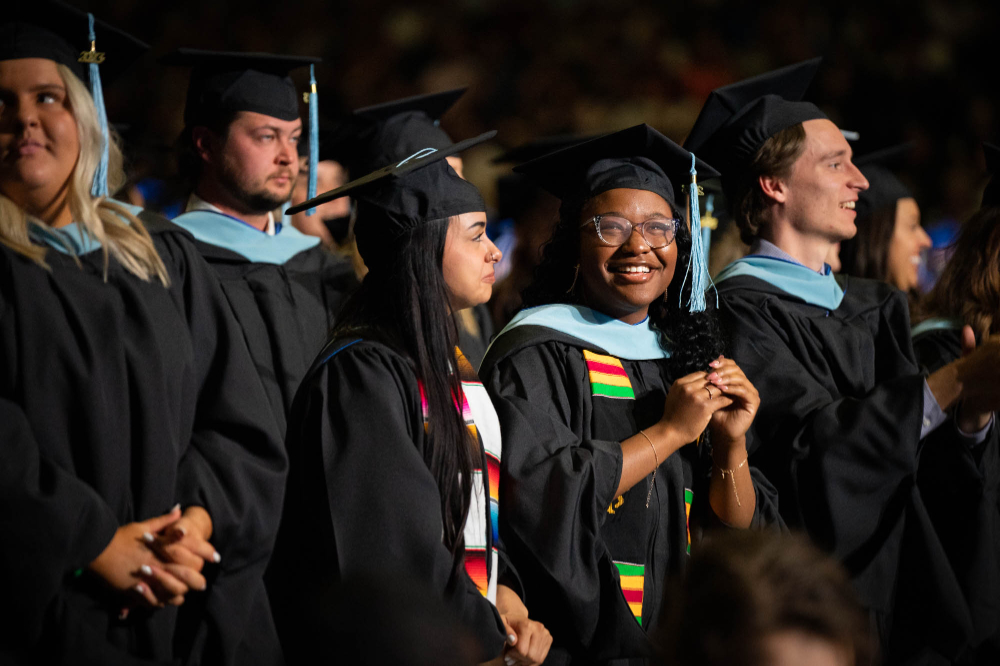 students in commencement regalia stand at their seats
