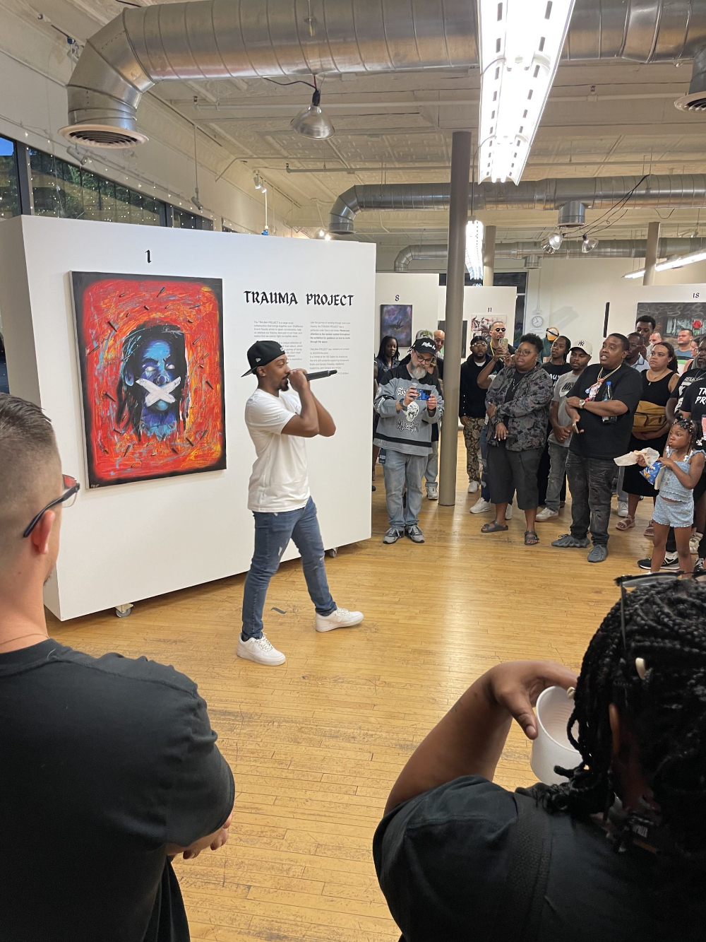 artist with microphone in front of Trauma Project display at art gallery