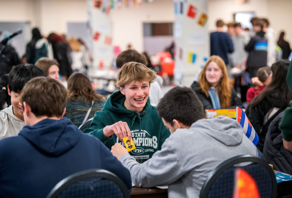 student in green sweatshirt plays game and holds yellow card out for others to see