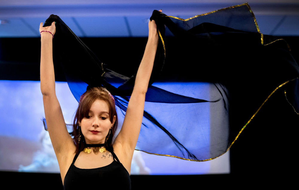 student with arms raised doing belly dance holding sheer fabric over her head