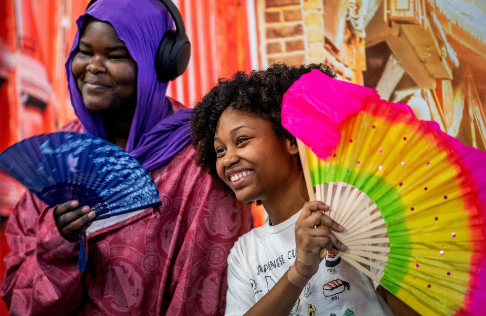two young students hold colorful fans while posing with photo booth props