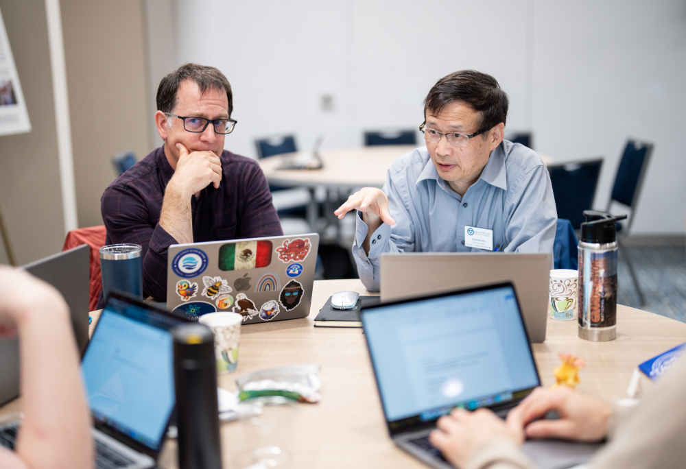 four open laptops, two men in back of table in focus