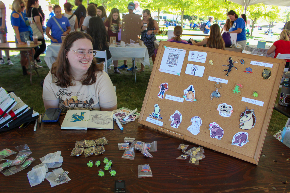 student sits in front of table with stickers she made, a cork board displays more