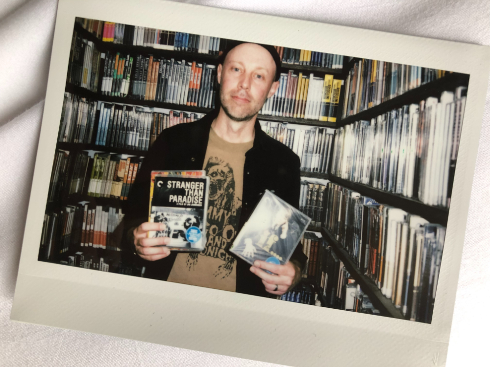 Joel Potrykus holds DVDs of movies in a closet filled with shelves of DVDs