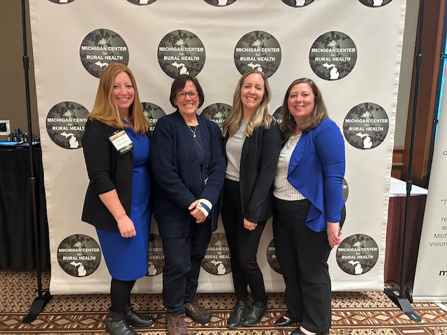From left are Shannon Owen, Theresa Bacon-Baguley, Kelly Aubry and Jenny Baweja in front of a backdrop at the Michigan Rural Health Conference in Mount Pleasant.