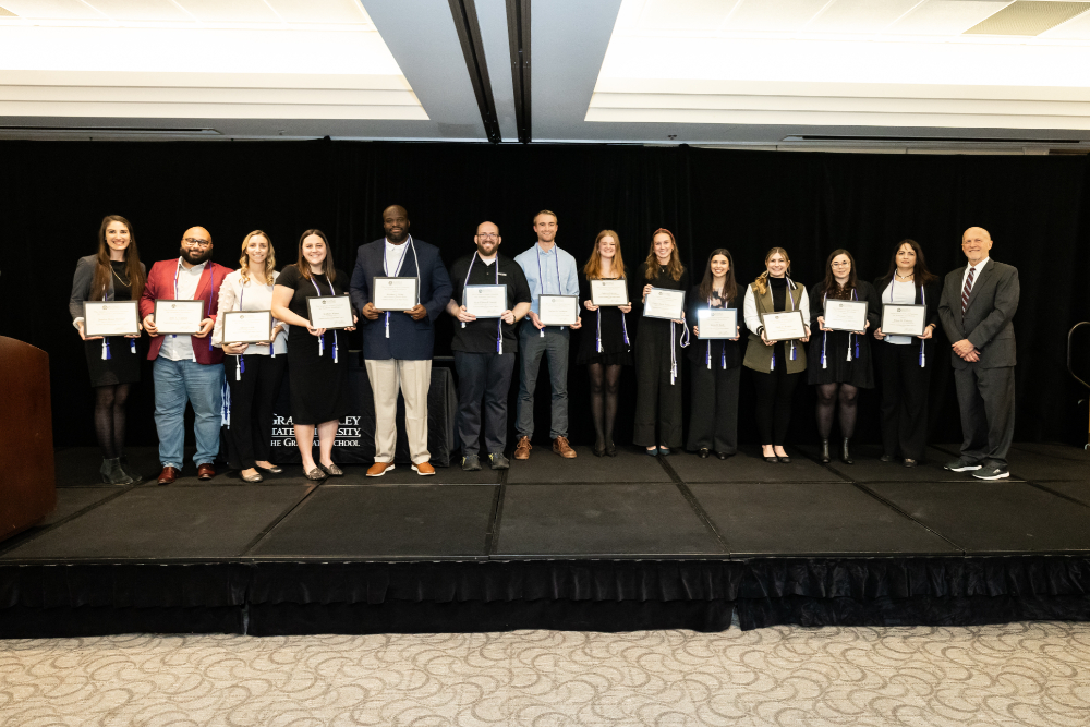long row of graduate students on stage holding certificates at ceremony