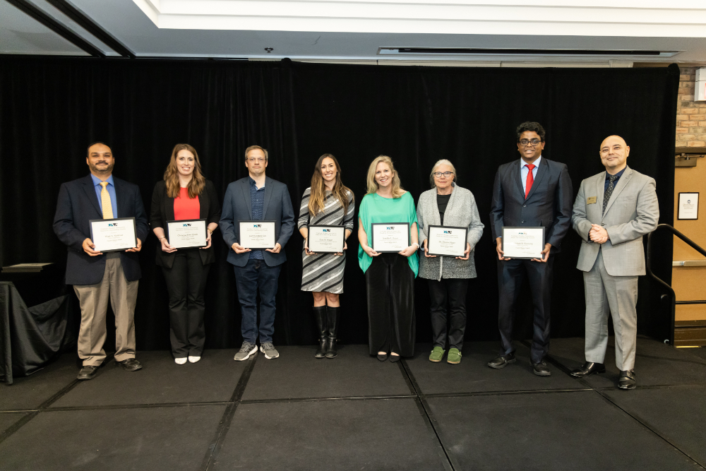 seven people holding certificates, man at far right standing in suit
