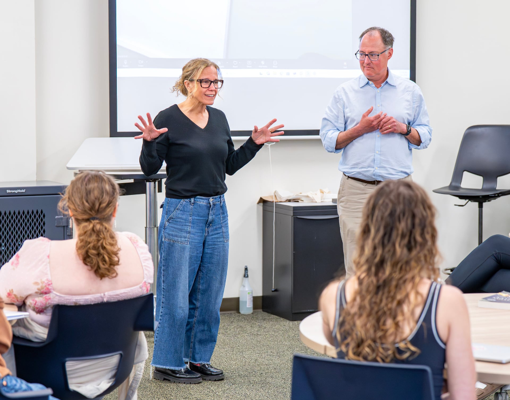Ellen Adams and David Eick stand before students in class