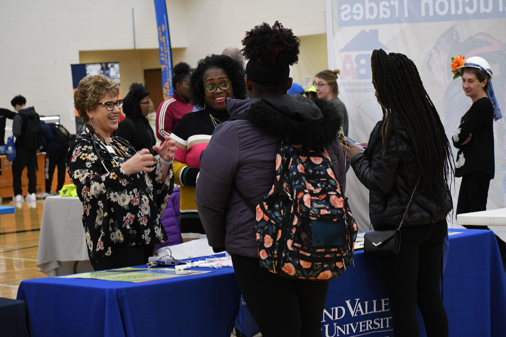 at a tabling event, two GVSU staff talk with two high school students, who are wearing coats