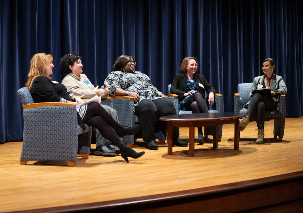 five women sitting on chairs on stage, smiling and laughing