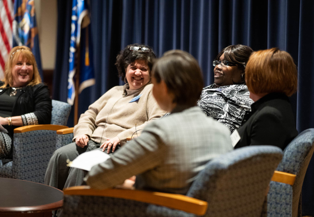 five women seated in chairs on a stage