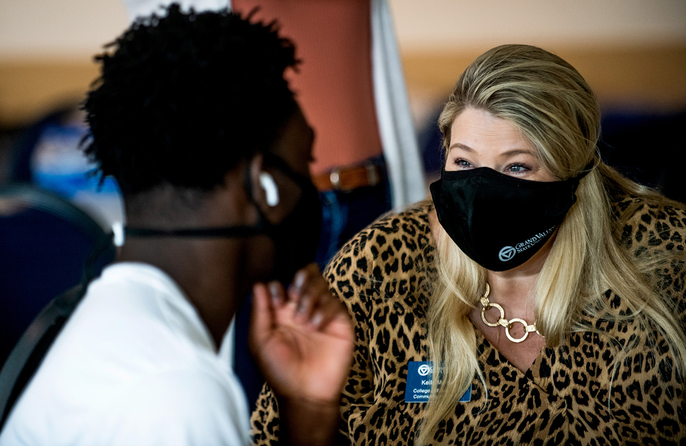 student in face mask sitting and conversing with faculty member in face mask
