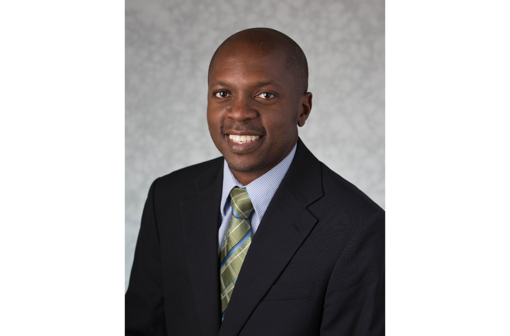 Babasola Fateye in dark suit jacket, light blue shirt with green tie with stripes