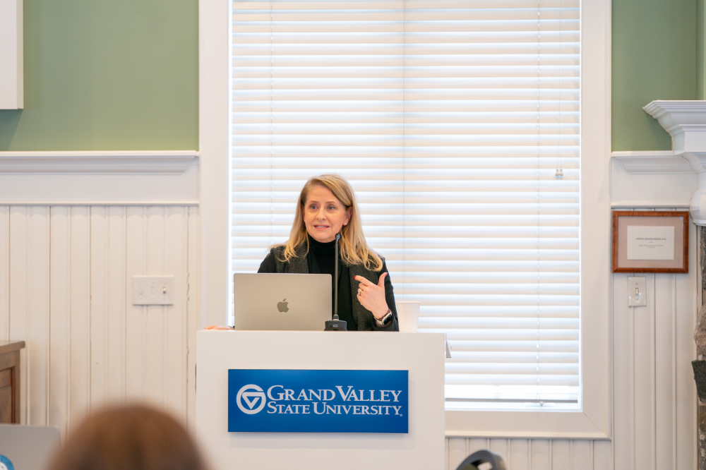 Stacie Behler speaks from a podium at the Alumni House, open laptop in front