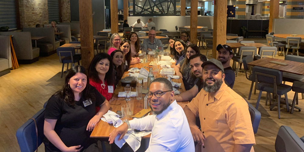 large group around a rectangle restaurant table, everyone smiling at camera