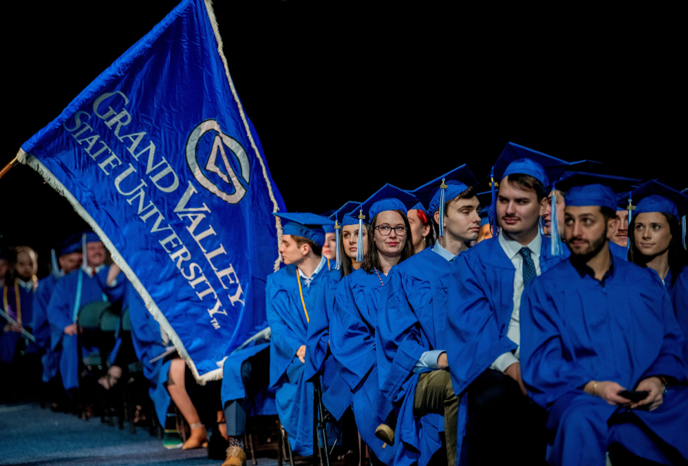 rows of graduates in blue robes with GVSU flag coming down center aisle
