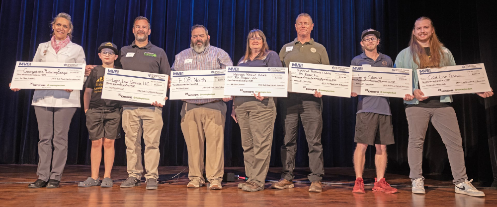 eight people standing on stage holding oversized checks