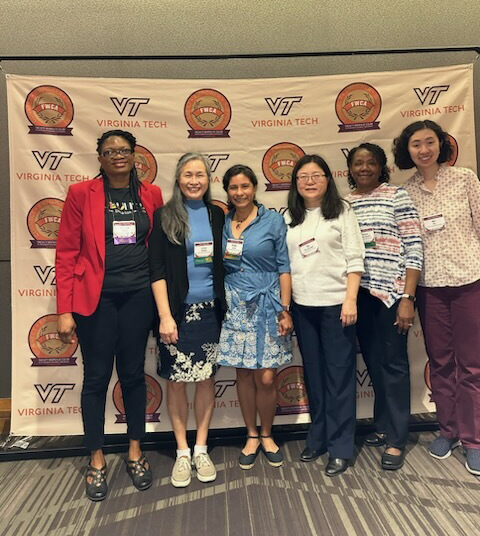 six women are standing against a backdrop of Virginia Tech