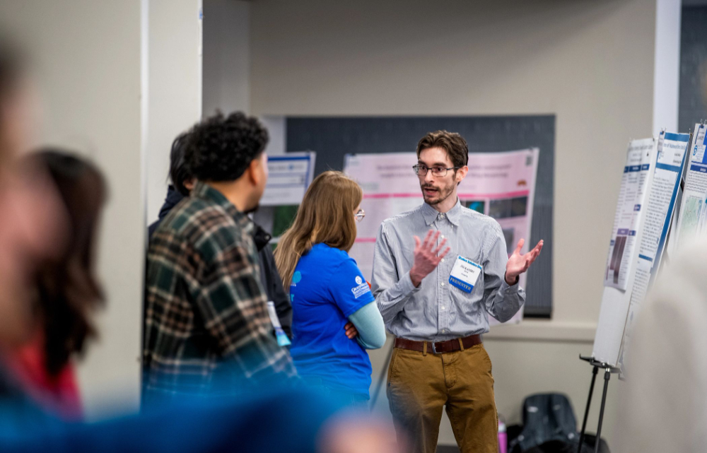 poster presentation with student explaining reserach to three people looking on