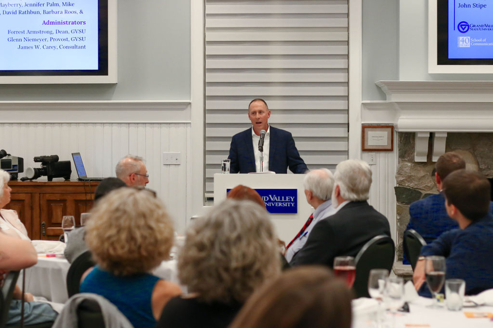 Keith Donovan speaks from a podium; people seated at tables at the Alumni House