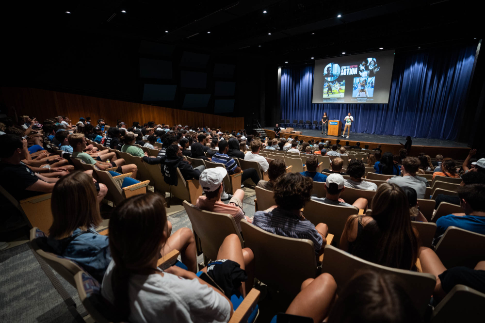people fill an auditorium to listen to keynote speakers on stage