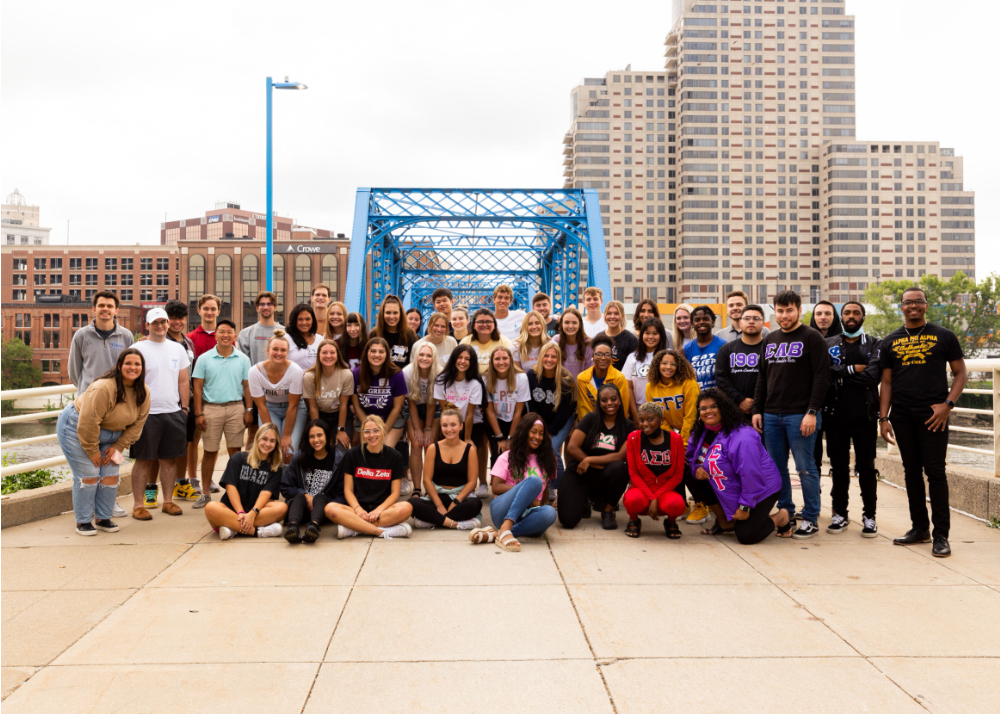large group of people, many in Greek shirts, jackets and sweatshirts are pictured on the blue bridge in Grand Rapids