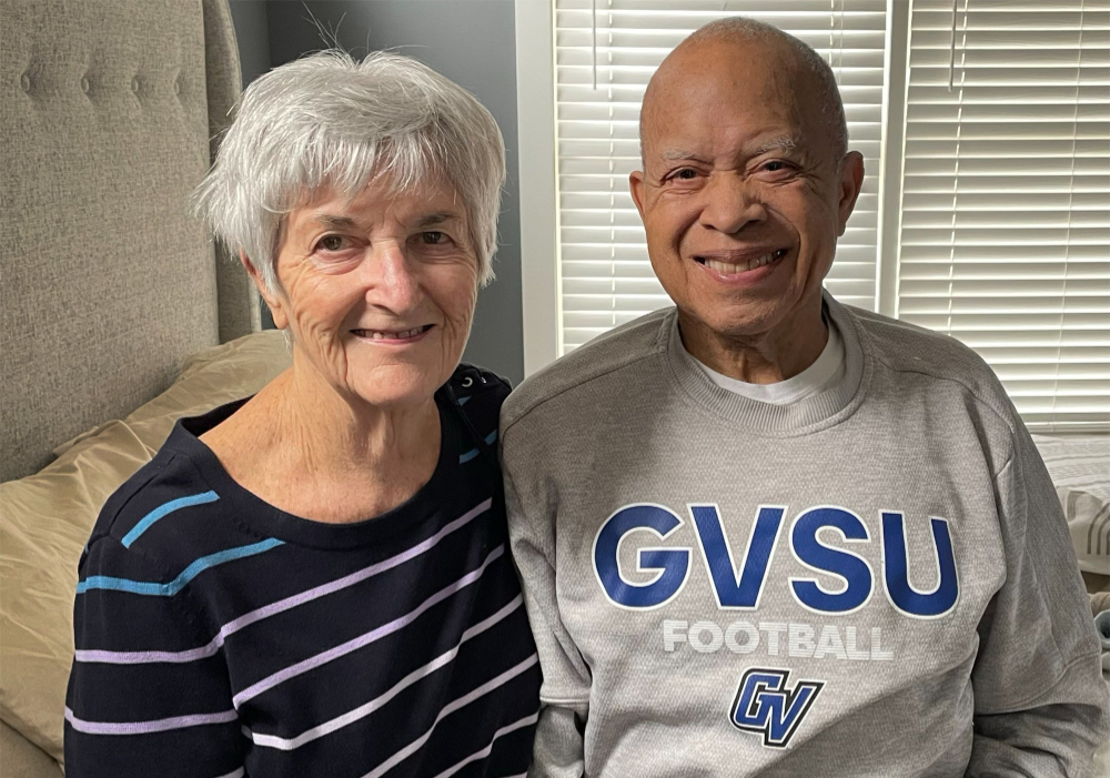 Constance and Curtis Jones are seated together on a sofa; he wears a GVSU football sweatshirt