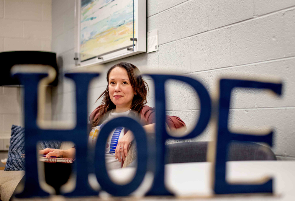 Elisa Ortega-Schultz sitted in a chair and looking through the letter o in a blue Hope sign placed on a table in front of her.