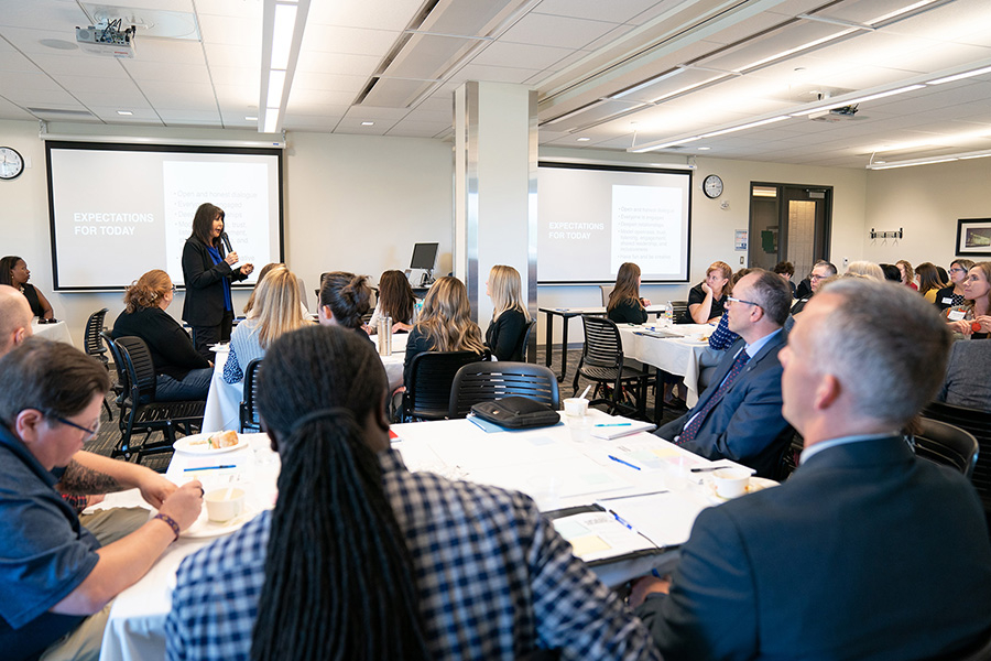 President Philomena V. Mantella uses a microphone to talk to a large room of people seated at round tables.