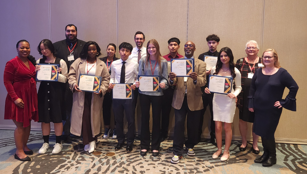 13 people standing in staggered row, eight people hold certificates