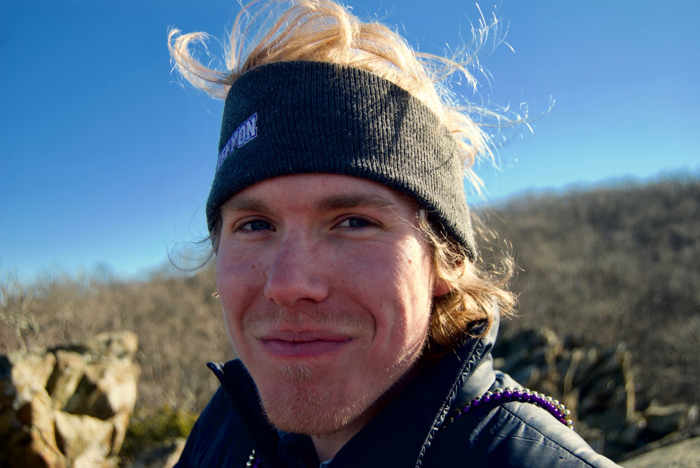 outdoor selfie of Isak Davis in black jacket, headband pushes up his blond hair