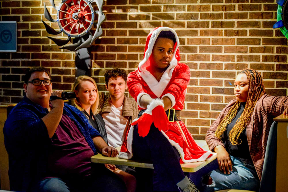 five students seated at table, one in red Santa outfit sitting on table