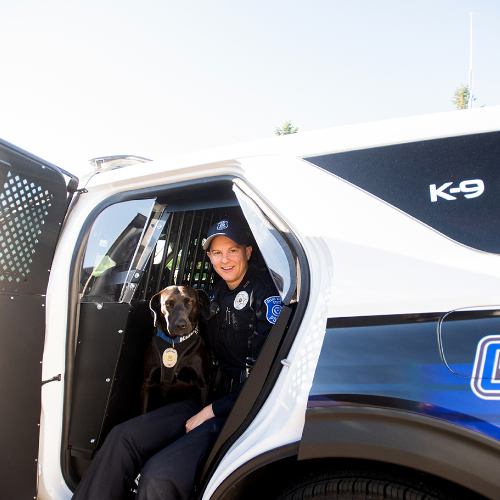 police officer and K-9 dog sitting in a new police SUV cruiser with K-9 Unit and GV as decals in back rear panel