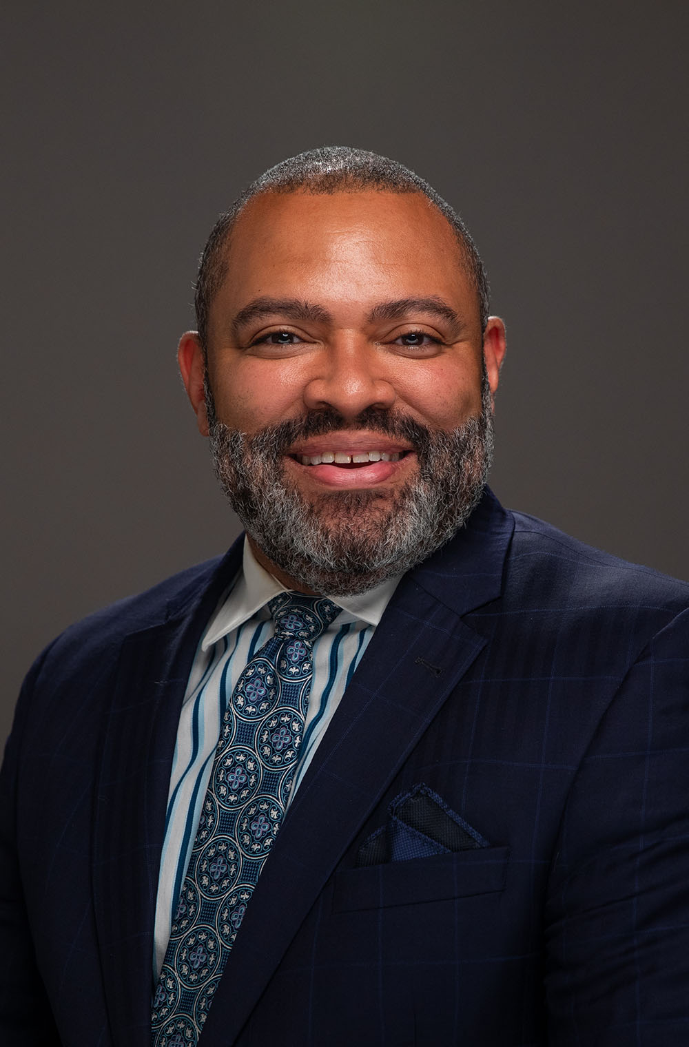 H. Julian Woods seated for portrait in dark blue suit jacket, striped shirt