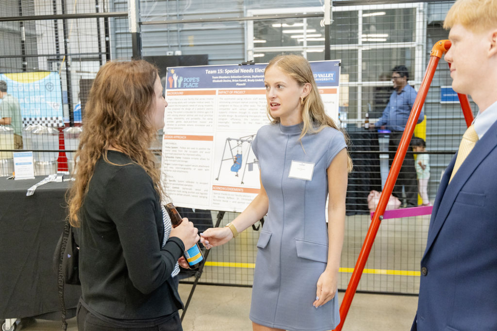 Grace Piasecki, center, in blue dress talking to another woman, and man stands at right